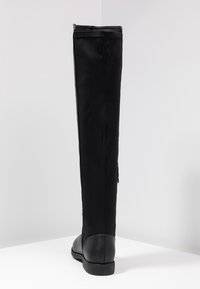 Bota plana negra hasta la rodilla con puntera redondeada y material superior liso, fotografiada sobre un fondo blanco liso.