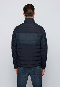 Pohodlná tmavě modrá bunda s vysokým límcem, s vodorovnými prošívanými částmi a kontrastní hladkou horní částí.