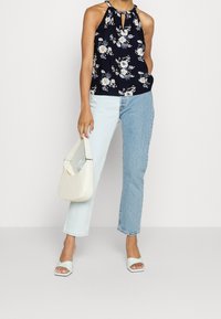 Haut halter à imprimé floral bleu marine avec ouverture en clé; jeans en denim bleu clair et bleu moyen; sac à main blanc; sandales à glissière vert menthe.
