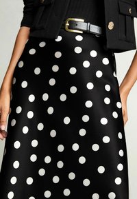 Musthave mustriline polka dot seelik, millel on suured valged täpid, valmistatud sileda ja läikiva kanga järgi. Seelikut täiendab must vöö kuldse pandlaga.
