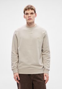 Μπεζ φούτερ με στρογγυλή λαιμόκοψη, μακριά μανίκια, απαλή υφή, ριμπ μανσέτες και τελείωμα, με μικρό μοτίβο λογότυπου στο στήθος.