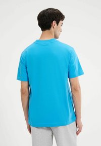 Camiseta de manga corta de algodón azul brillante con cuello redondo clásico y un corte relajado. Diseño minimalista, sin logotipos ni patrones visibles.