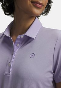 Ανοιχτό μοβ πόλο με γιακά με κουμπιά, διακοσμημένο με μικρό λογότυπο στο στήθος, κατασκευασμένο από απαλό, αεριζόμενο ύφασμα.