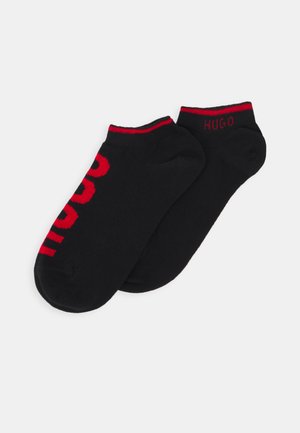 Chaussettes noires de cheville avec des accents rouges ; la chaussette gauche présente 'HUGO' en lettres grasses et un poignet rayé rouge contrasté. Tissu doux en tricot.