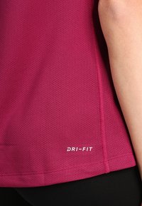 Camiseta de manga corta, de secado rápido en fucsia, con textura de malla y logo "DRI-FIT" cerca del dobladillo.