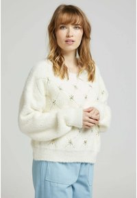 Pull oversized blanc et duveteux avec des motifs en forme de diamant et des accents d'étoiles dorées. Poignets et ourlet côtelés. Assorti à un pantalon bleu clair.