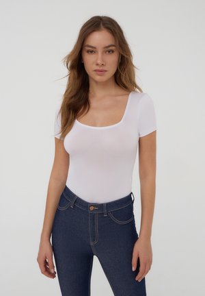 Body bianco a maniche corte con scollatura quadrata, abbinato a jeans blu scuro a vita alta con tasche e dettagli di cucitura.