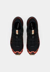 Scarpe da ginnastica nere con dettagli arancioni, caratterizzate da una tomaia testurizzata, sistema di allacciatura e suola robusta. Logo ben visibile sulla linguetta.