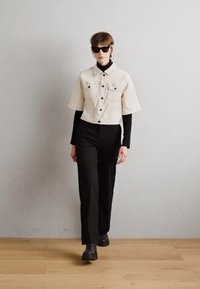 Avklippt beige denimjacka med korta ärmar, två bröstfickor, matchad med en svart långärmad topp och svarta vida byxor, bärs med svarta stövlar.