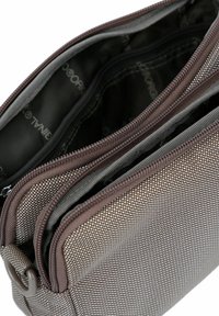 Bolsa de tela marrón con múltiples compartimentos con cremalleras, que presenta un patrón de malla y un forro interior suave en tonos grises.