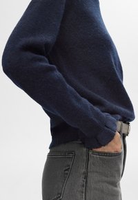 Temno modri pleteni pulover z razpotegnjeno prileganjem, rebrastimi manšetami in mehko teksturo, kombiniran z sivimi kavbojkami s sprednjim žepom.