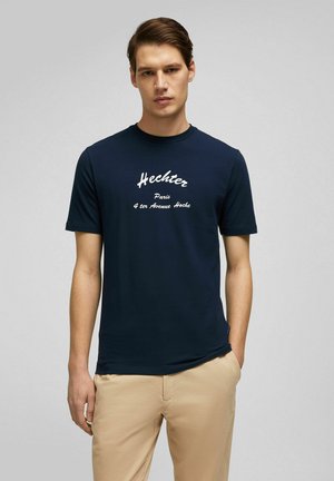 Navyblaues T-Shirt mit kurzen Ärmeln aus Baumwolle, das auf der Vorderseite weißen Text "Hechter Paris 4 ter Avenue Hoche" trägt. Glatte Textur.