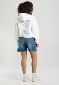 White hoodie with blue graphic of a cocktail glass and text on the back, paired with blue denim shorts. Casual fit, medium length.