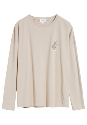 Chemise beige à manches longues avec un petit motif floral noir et le mot "COLLECTED" sur le côté gauche de la poitrine.