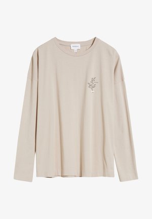 Chemise beige à manches longues avec un petit motif floral noir et le mot "COLLECTED" sur le côté gauche de la poitrine.