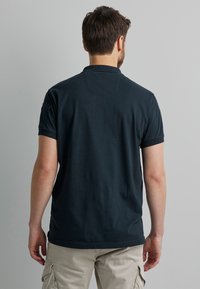 Navyblaues Polohemd aus Baumwolle. Hat ein schlichtes Design, kurze Ärmel und einen umgeschlagenen Kragen. Die Rückansicht zeigt ein dezentes Rückenpasse-Detail.