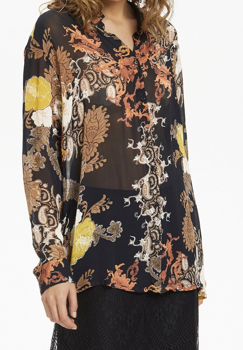 Blusa a maniche lunghe, con bottoni, in tessuto nero trasparente con motivi floreali e paisley in arancione, giallo e bianco. Tessuto morbido, vestibilità comoda.