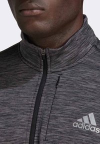 Veste grise à fermeture éclair avec col haut, fabriquée en tissu texturé. Dispose d'une fermeture éclair noire et d'un logo Adidas blanc sur la poitrine.