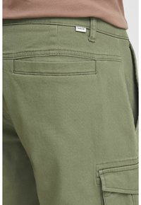 Olivenbrune cargo bukser lavet af bomuld, med en lappetaske på siden og en stitched talje med et mærkat.