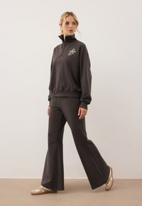 Donkergrijze zip-up sweatshirt met geborduurd bloemenontwerp, gecombineerd met bijpassende flared sweatpants en beige sneakers. Gladde stofstructuur.