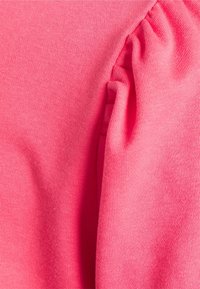 Pink cotton fabric with a soft texture, featuring gentle gathers and subtle stretch. Close-up reveals fine knit pattern.