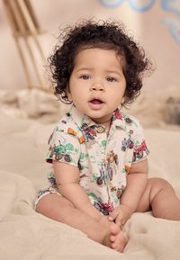 Robe courte de couleur claire avec des motifs de tracteurs colorés, manches courtes et encolure boutonnée, texture de tissu douce et coupe décontractée.