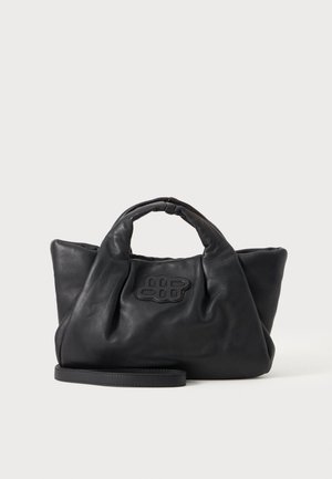 Sac à main en cuir souple noir avec de courtes poignées, une bandoulière amovible et un logo cousu à l'avant, sur un fond uni clair.