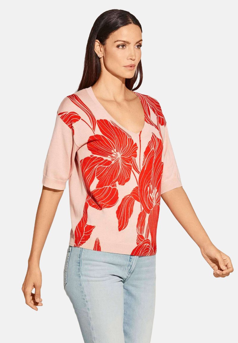 Rosa Kurzarmpullover mit einem lebhaften roten Blumenmuster und einem V-Ausschnitt. Das Material wirkt glatt mit einer leichtgewichtigen Textur.