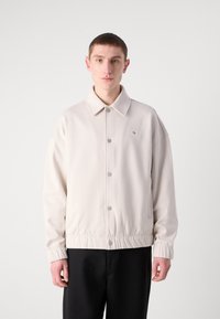 Giacca beige chiaro con colletto, bottoni a pressione sul davanti, polsini elasticizzati e design slim fit. Caratterizzata da un piccolo logo sul petto.