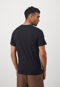 Black cotton t-shirt with short sleeves and a crew neck, smooth texture, displayed from the back, paired with brown checkered shorts.