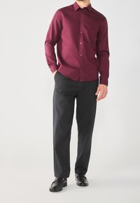 Chemise à manches longues bordeaux avec un design à boutons, associée à un pantalon noir et des chaussures noires. Tissu lisse, coupe cintrée.