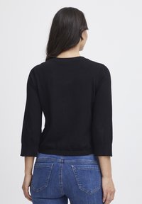Svart stickad tröja med trekvartsärmar, rund hals och en enkel struktur. Kombinerad med åtsittande blå denimjeans.