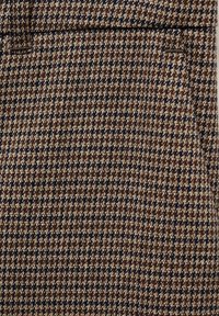 Tissu marron et noir à motif pied-de-poule avec une poche passepoilée horizontale près du centre supérieur.