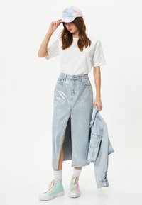 Ljusblå denim maxi kjol med en främre slits, tillsammans med en vit t-shirt och pastellfärgad tie-dye keps. Bärs med pastellfärgade sneakers i hög modell.