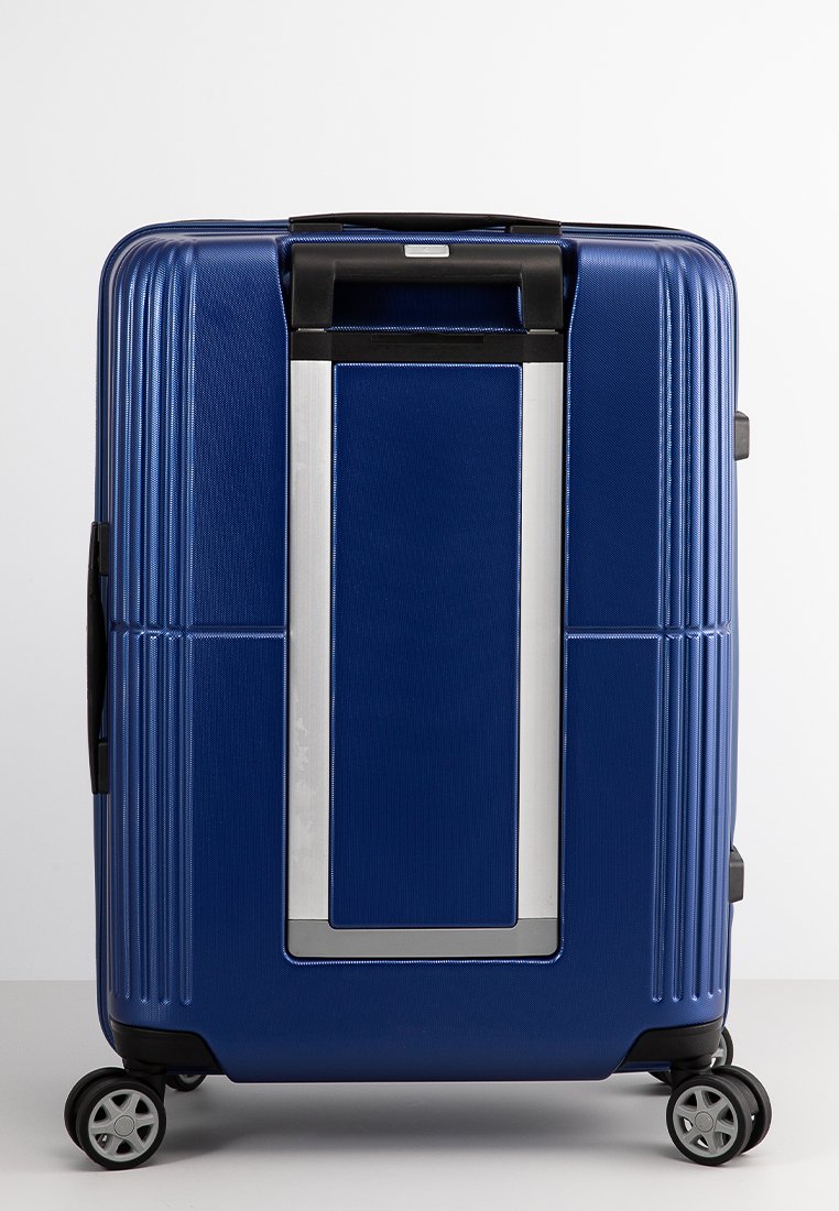 Maleta rígida azul con superficie texturizada, estrías horizontales, mango retráctil y cuatro ruedas giratorias para movilidad. Incluye detalles en plata.