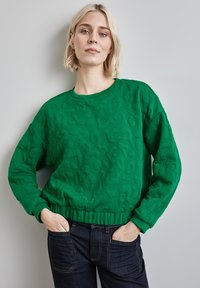 Grüne Sweatshirt mit strukturiertem Muster, Rundhals-Ausschnitt und elastischem Saum. Kombiniert mit dunkelblauen Jeans. Leichtes Material.