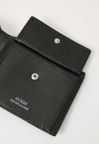 Black leather wallet with a snap closure, featuring a smooth texture and silver hardware. "GUESS GENUINE LEATHER" printed on the interior.