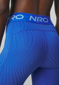 Niebieskie legginsy sportowe z teksturowanym wzorem w zygzak. Posiadają szeroką, elastyczną talię z napisem "NIRO" w kontrastującym białym kolorze.
