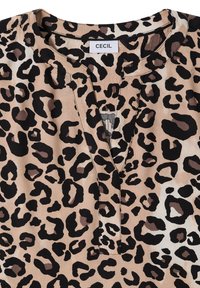 Vêtement beige avec un motif léopard noir et brun foncé et un col en V avec une petite étiquette blanche portant la mention "CECIL".