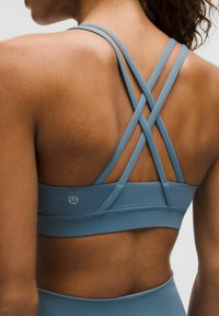 Brassière de sport en tissu bleu doux à la texture lisse, avec un design à bretelles croisées dans le dos et un marquage discret sur la bande.