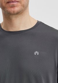 Pilkas trumpas rankovėmis marškinėliai, pagaminti iš lygios medžiagos. Yra apvalus iškirpimas ir mažas baltas logotipas kairėje krūtinės pusėje.