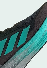 Black athletic shoe with teal accents, featuring textured upper, three stripes logo, and a lightweight sole with a patterned design.