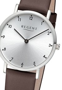 Montre ronde en argent avec un cadran argenté en forme de rayon de soleil, marqueurs d'heure noirs et bracelet en cuir brun. Le nom de la marque "REGENT" est affiché.