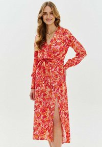 Dlhé rukávy, zavinovacia sukňa s kvetinovým vzorom v oranžových a ružových odtieňoch. Má hlboký V-výstrih a bočný rozparok. Tkanina vyzerá ľahko a voľne.