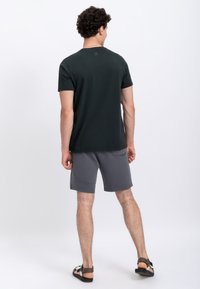 Donkergroen T-shirt met korte mouwen, gecombineerd met grijze shorts met gestructureerde stof en zakken, gezien vanaf de achterkant.