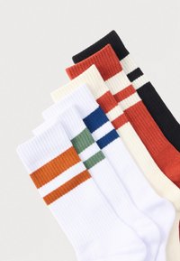 Έξι ζεύγη ριγωτές κάλτσες με δύο οριζόντιες ρίγες σε κάθε ζευγάρι, τα χρώματα περιλαμβάνουν λευκό με πορτοκαλί, λευκό με πράσινο, λευκό με μπλε, εκρού με πορτοκαλί, πορτοκαλί και μαύρο με λευκό.