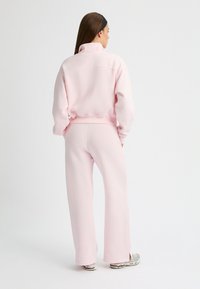 Lichtroze, oversized sweatshirt met een hoge kraag, geribbelde zoom en bijpassende wijde broek. De stof lijkt zacht met een nette afwerking.
