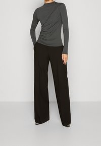 Långärmad, figurnära grå topp med samlat tyg på ena sidan, i kombination med högmidjade svarta vida byxor och spetsiga klackskor.