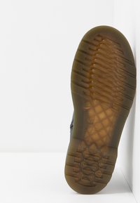 Svart skosula med en texturerad gummiyta, som har ett geometriskt mönster och spår för grepp, som övergår till en genomskinlig brun nyans.