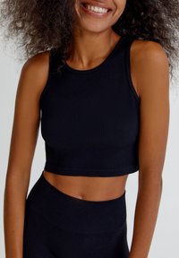 Top corto negro de canalé con escote redondo y diseño ajustado, combinado con pantalones de tiro alto a juego, creando un look sin costuras.